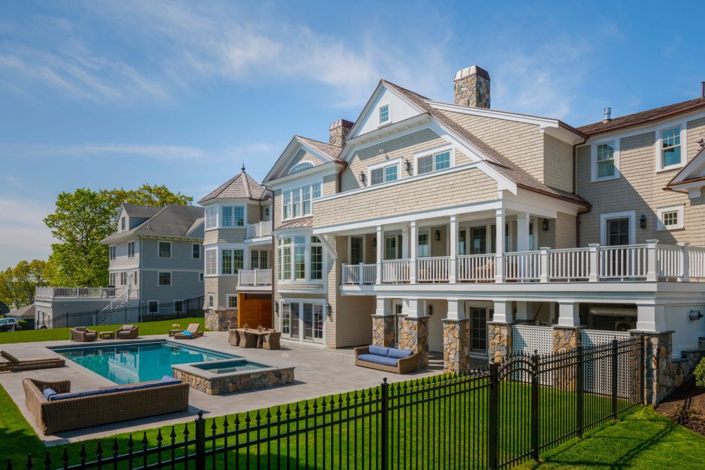 Backyard view of a shingle-style home with large pool, patio, and outdoor lounge space in Hingham, Massachusetts