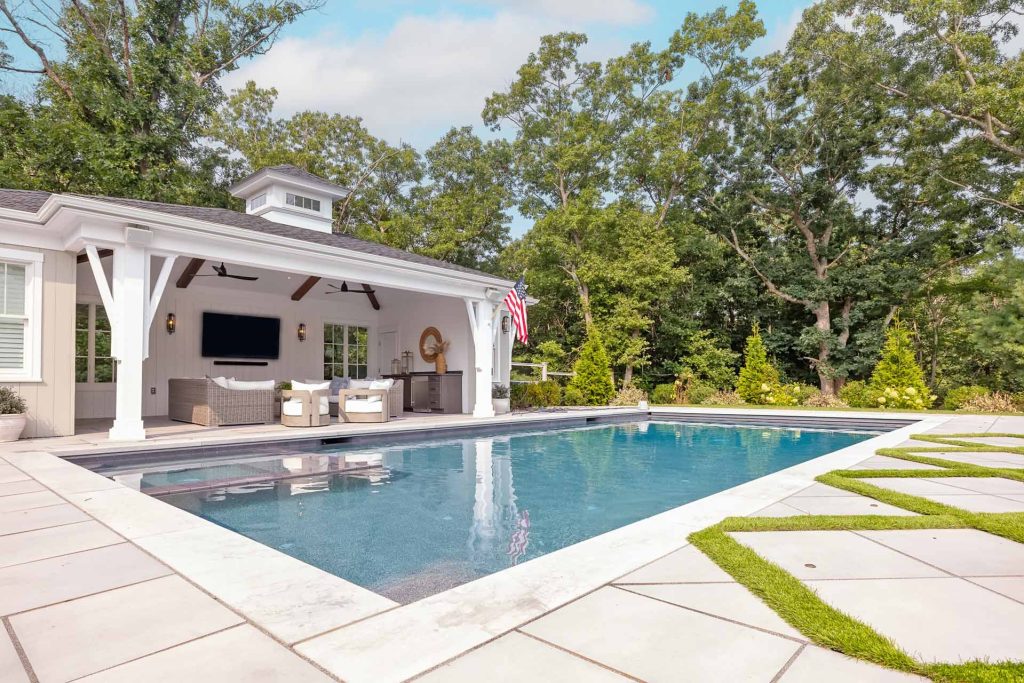 The pool house's covered porch, wrapped in white columns, reflects across the pool at the heart of the property's outdoor living space.